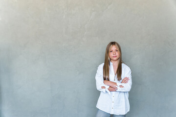 young girl with crossed arms in front of a gray wall.