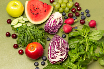 Two halves of blue cabbage, an apple, bunch of arugula, sprigs of green basil and berries.