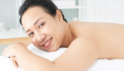 Obraz premium Smiling Asian woman lying on bed while undergoing acupuncture treatment