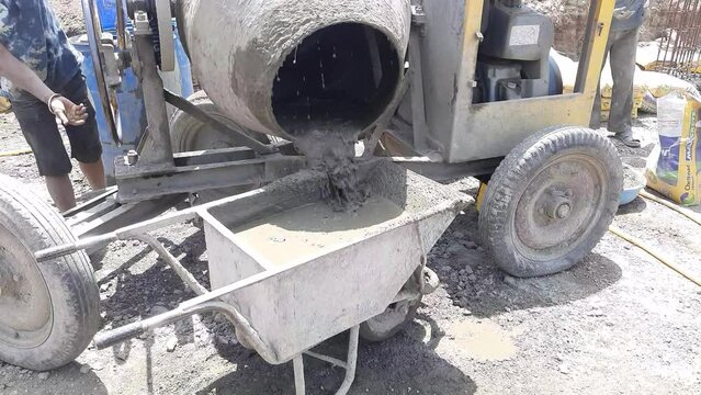 A close-up view of an diesel concrete mixer pouring wet cement into the wheelbarrow at the construction site in India