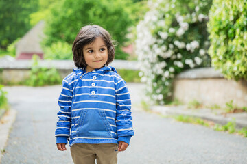 Little eastern handsome baby boy staying outdoor in old town in France. Boy wearing blue jacket