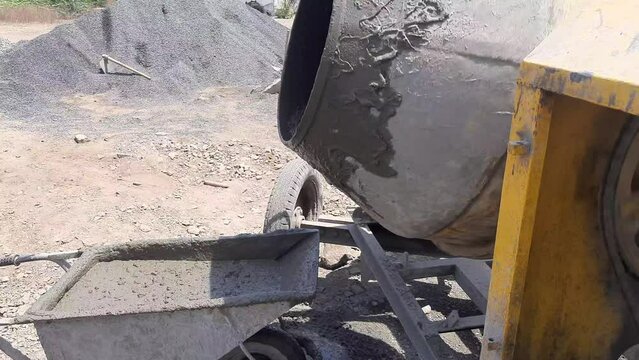 A close-up video shot of an electric concrete mixer pouring wet cement into the wheelbarrow