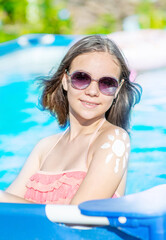 Happy teen girl with sun protection cream on her skin spends time  in the pool