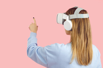 Woman in VR glasses explore new horizons with finger. Girl in virtual reality headset isolated on pink studio background touch air with hands discover cyberspace. Technology concept.
