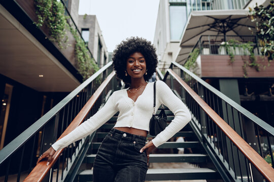 Young smiling african woman poses near stairs in the city