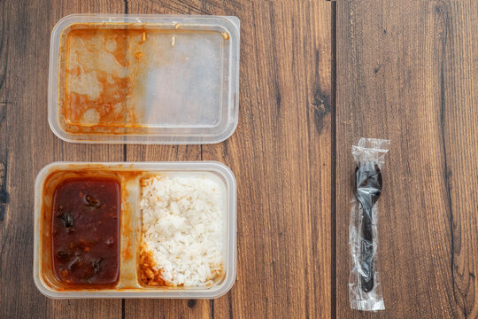 Fast food in a plastic container and small plastic fork on a wooden table. Budget business lunch. One side with arbecue
chicken and second with jasmine white rice. Eat on a go concept. 