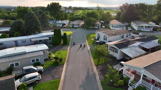 Elderly women ride jazzy scooter wheelchairs outside through old income housing rural mobile home park in USA. Friends enjoy old age together.