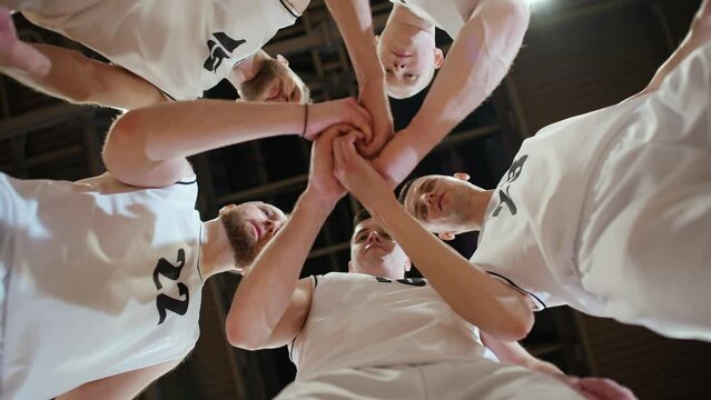 Slow motion, team of basketball players shouts chants and raising morale before the game, the international basketball championship, view from the lower angle.