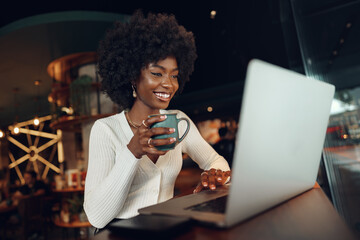 Smiling young african woman sitting with laptop in coffee shop