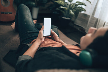 Men hand holding texting  mobile phone with blank screen and wearing headphone on sofa at home. Relax home concept.