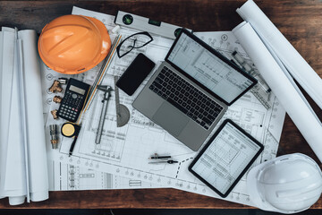 Laptop and tablet with drawings inspection on the office desk and Calculator, triangle ruler, safety glasses, compass, vernier caliper on Blueprint. Engineer, Architect, Industry and factory concept.