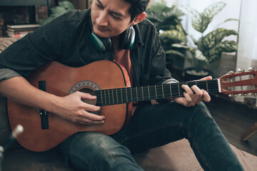 young man relax and playing guitar while sitting on sofa bed in living room at home.