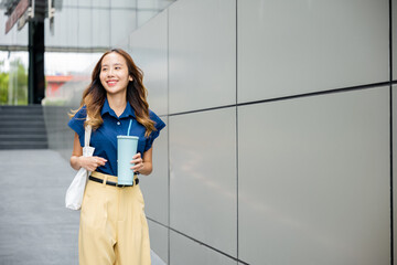 Obraz na płótnie Canvas Asian beautiful business woman confident smiling with cloth bag holding steel thermos tumbler mug water glass she walking outdoors on street near modern building office, Happy female looking side away