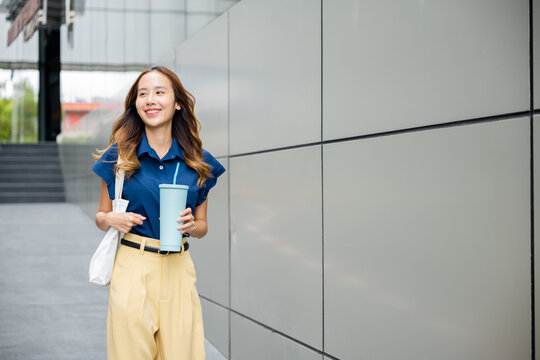 Asian Beautiful Business Woman Confident Smiling With Cloth Bag Holding Steel Thermos Tumbler Mug Water Glass She Walking Outdoors On Street Near Modern Building Office, Happy Female Looking Side Away