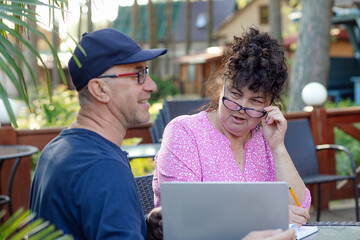 Portrait of middle-aged couple. Curly woman looking suspiciously at smiling man sitting near laptop...