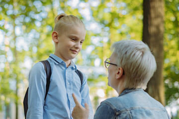 cute caucasian blonde boy with ponytail going to school. Mother having a conversation with child