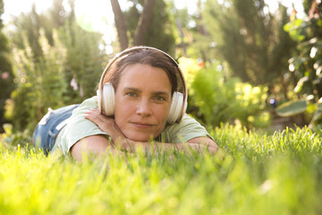 Audio healing. meditation. Slow life. Enjoying the little things. middle aged woman wearing headphones listens to music lying on the grass outdoor. 