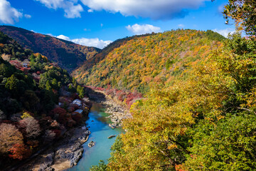 秋の京都・嵐山公園の亀山展望台から見た、紅葉に彩られた山の間を流れる桂川と背景の青空