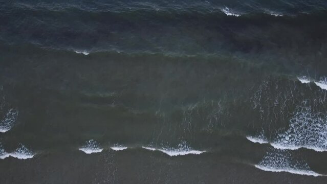 Waves crash towards shore during an overcast day.