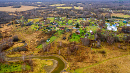 Aerial view of the village on a high hill above the river at sunrise in autumn. Aerial view. Residential buildings and a church, river bends, meadows, orange grass, trees at dawn. 