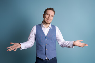 Portrait handsome business man with charming smile, gesturing with his hands while standing at casual post as if talking on a blue background. Caucasian guy leads successful negotiations