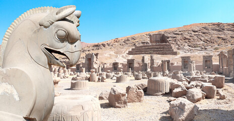 Fototapeta premium Stone sculpture of griffin and Ruins of Palace of 100 columns and tomb of Artaxerxes III, Persepolis, Iran
