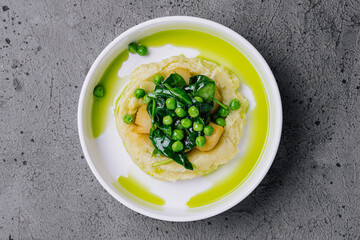 Mashed potato with butter, green peas, basil in a white bowl