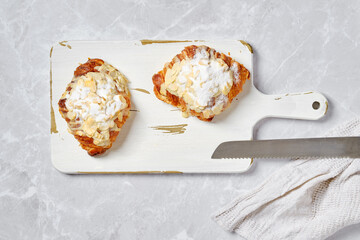 Overhead view of croissant with caramel and peanut shavings on white board on marble background