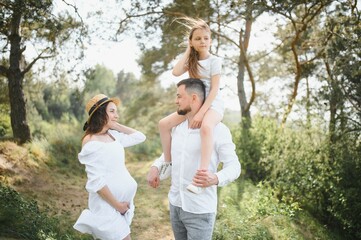 Naklejka na ściany i meble Happy pregnant couple with daughter in summer nature.