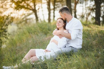 Naklejka na ściany i meble Happy and young pregnant couple hugging in nature