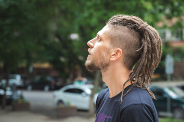 Side view of a caucasian man with dreadlocks and sidecut on a summer street.