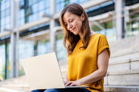 Smiling businesswoman using laptop sitting on steps