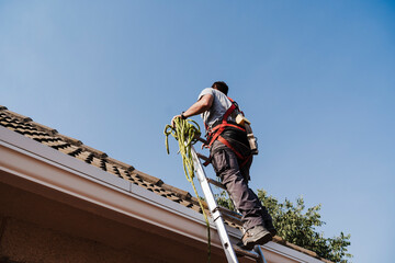 Technician moving up on ladder by house rooftop