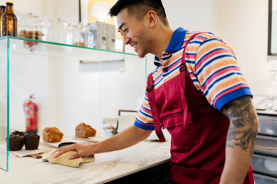 Smiling Man Cleaning Counter With Rag In Coffee Shop