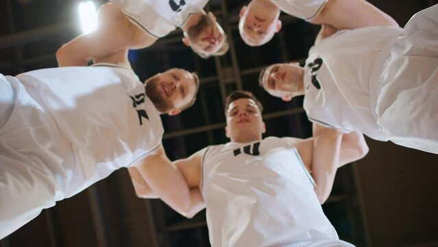 Slow motion, team of basketball players shouts chants and raising morale before the game, the international basketball championship, low angle view.