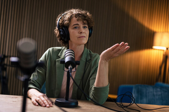 Presenter wearing headset gesturing sitting with microphone at radio station