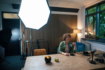 Smiling radio DJ sitting by strobe light with microphone at desk in recording studio