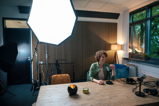 Smiling radio DJ sitting by strobe light with microphone at desk in recording studio