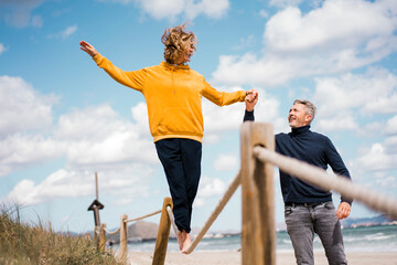 Mature man holding hand of woman assisting her walking on rope at beach