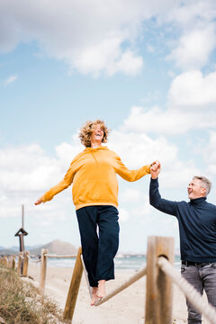 Happy woman holding hand with man walking on rope at beach