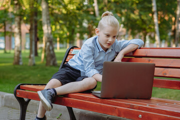 cute caucasian boy sitting on bench in park with laptop computer. Black screen