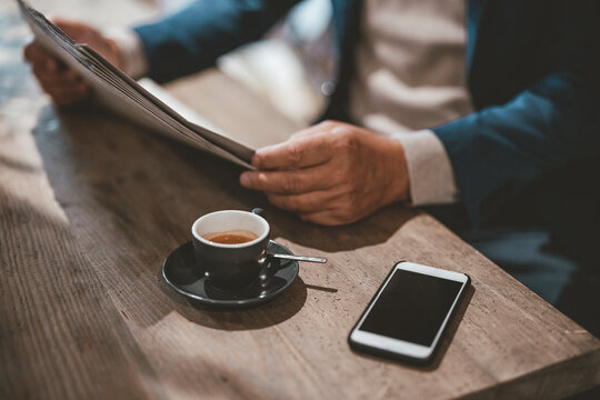 Businessman reading newspaper by coffee and smart phone at cafe - Powered by Adobe