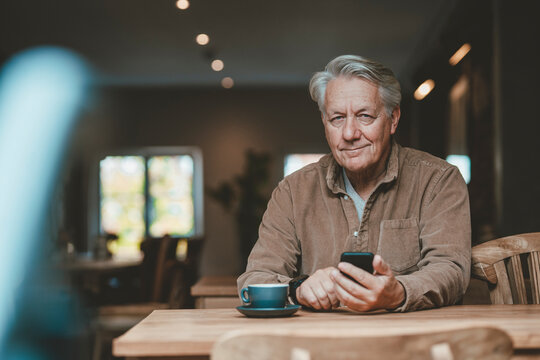 Smiling senior man with mobile phone in cafe - Powered by Adobe