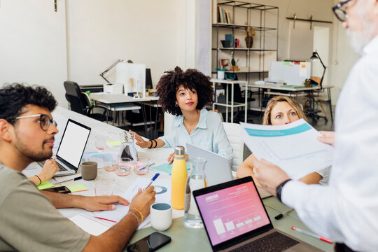 Multiracial workers looking at manager reviewing report in meeting at office
