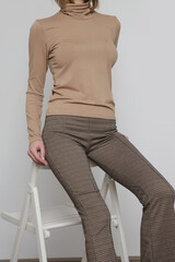 Serie of studio photos of young female model wearing beige turtleneck and skinny trousers. 