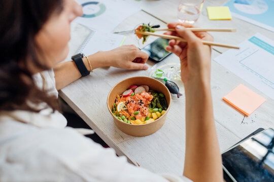 Businesswoman eating healthy poke bowl with chopsticks in lunch break at office