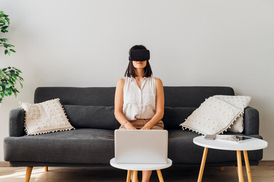 Woman using virtual reality glasses sitting on sofa at home