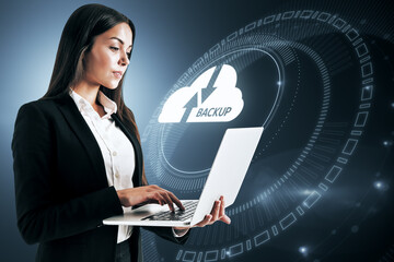 Attractive young european businesswoman holding laptop with abstract glowing cloud hologram on...