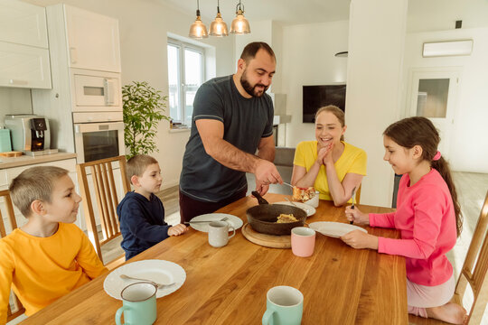 Smiling father serving breakfast to family at home