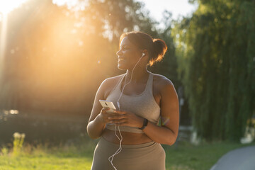 African American woman using mobile phone and earphones before exercising at the park in a  summer...